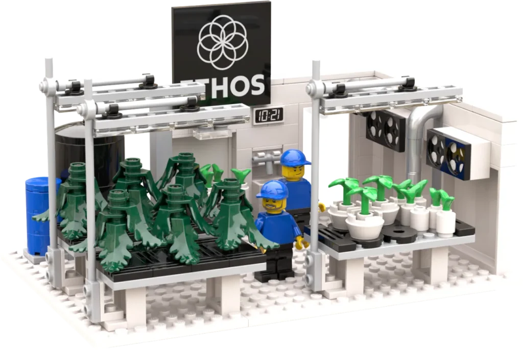 LEGO lab scene with two workers in blue helmets tending potted plants on a white table, surrounded by green trees and lab equipment under a ETHOS logo sign.